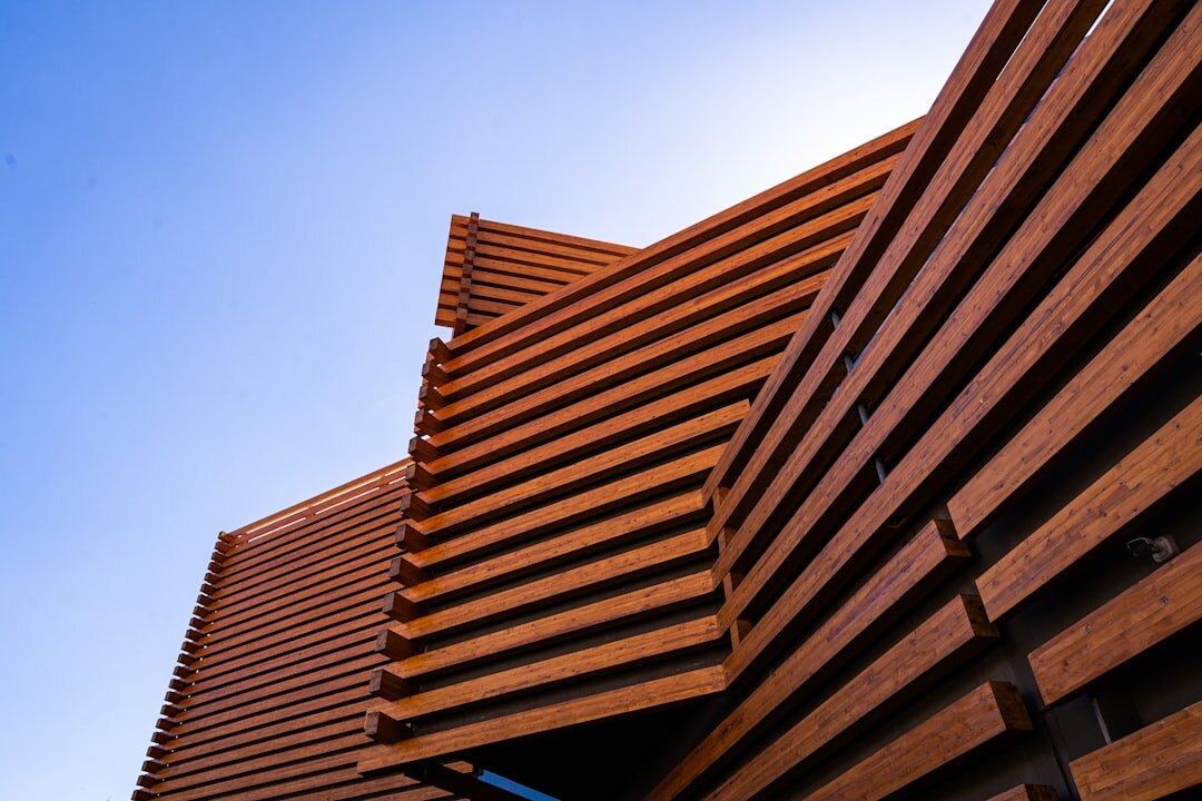 Detail of a modern oceanfront home facade with wood louvers and warm interior light at dusk